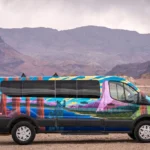 Colorfully painted Escape campervan parked in a desert landscape with mountains in the background.