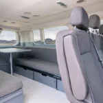 Interior of a campervan with rear bucket seats, bench seating, and a compact dining area.