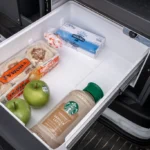 Campervan fridge drawer stocked with English muffins, apples, butter, and a bottled vanilla latte.