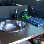 Stainless steel sink with a faucet inside the campervan kitchen, next to soap, sponge, and folded dish towels.