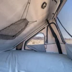 Interior of the rooftop sleeper tent on the Mesa campervan, with a mattress, mesh storage, and desert views through screened windows.