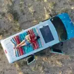 A woman playing the guitar while laying on the roof of an Escape Camper Van.