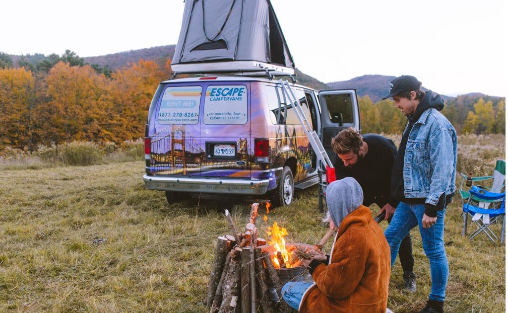 People sitting around a campfire with an Escape Camper Van on a Vermont road trip.