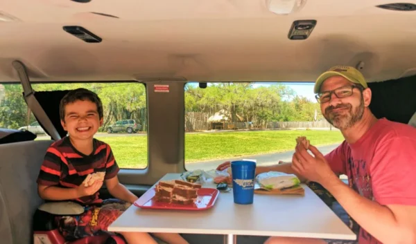 A dad and son eating a easy camping lunch inside a camper van.