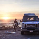 Escape Camper Van parked on a beach beside a surfer wit a surfboard
